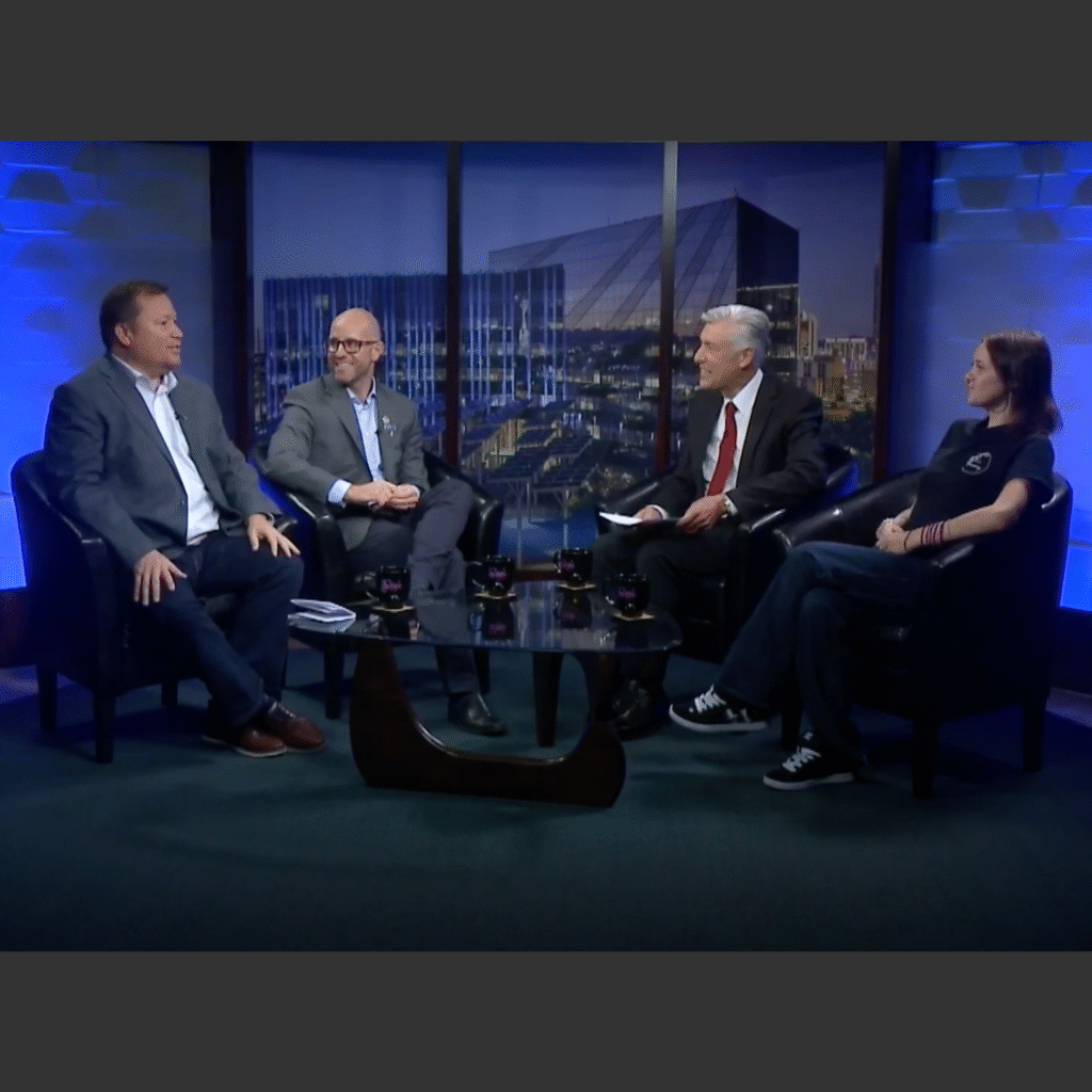 Three men and a woman sit on chairs for a TV interview.