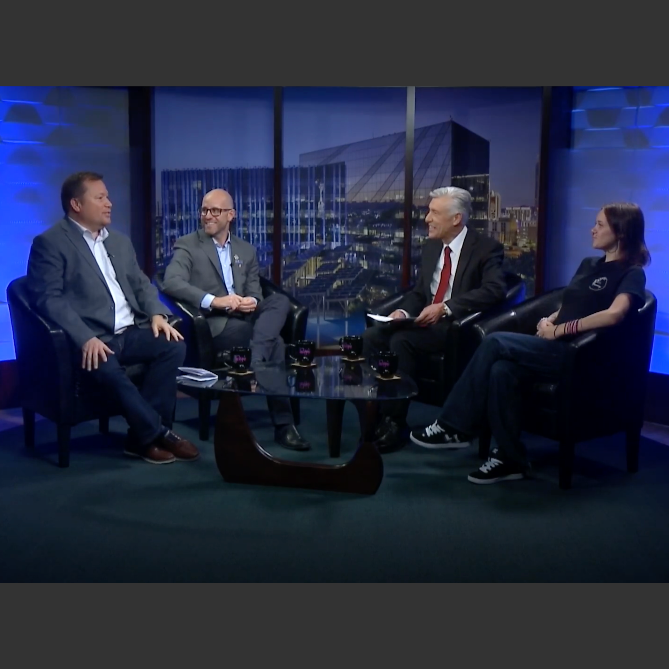 Three men and a woman sit on chairs for a TV interview.
