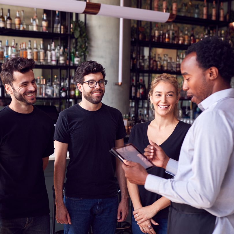 A group of restaurant servers receive training from a manager.